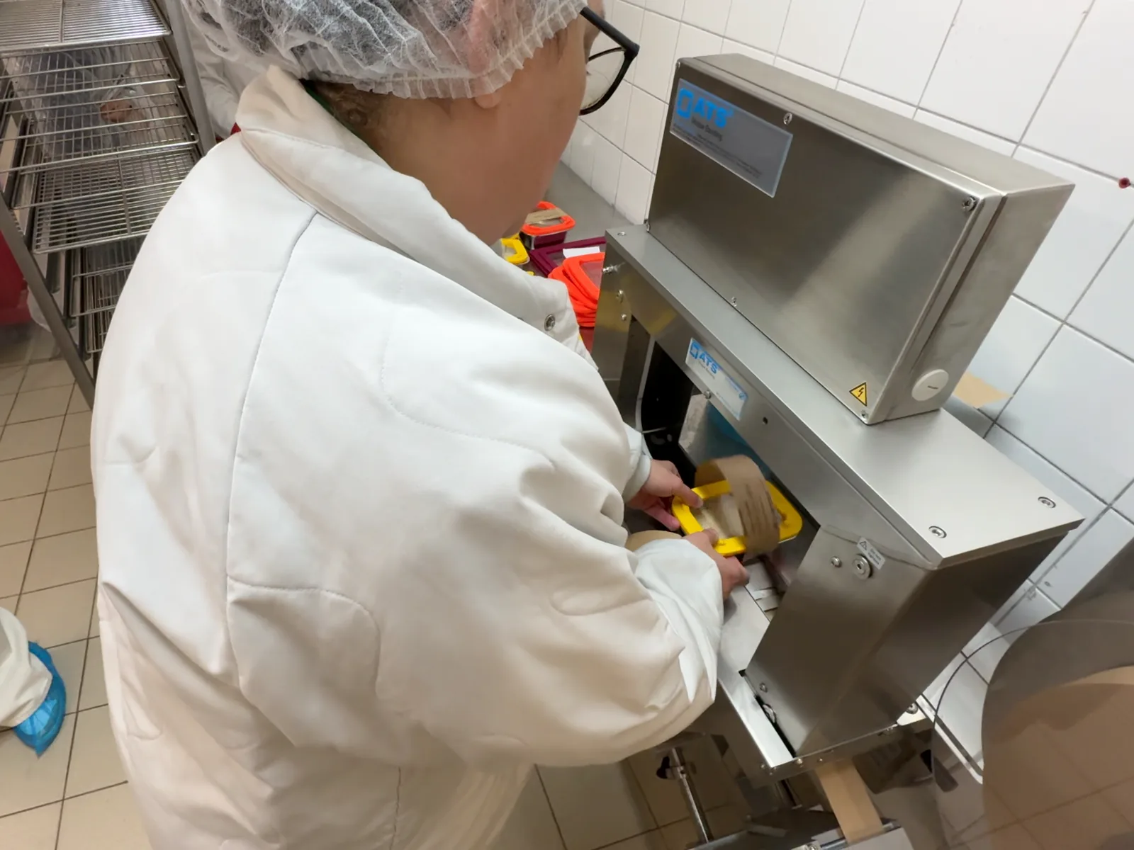 Opératrice posant un contenant dans la banderoleuse ATS, en cuisine centrale