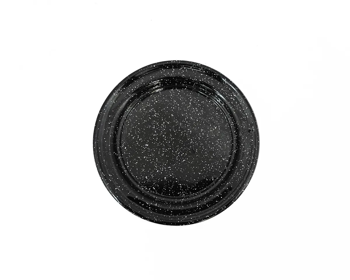 Assiette plate émaillée noire mouchetée de blanc, vue de dessus sur fond clair