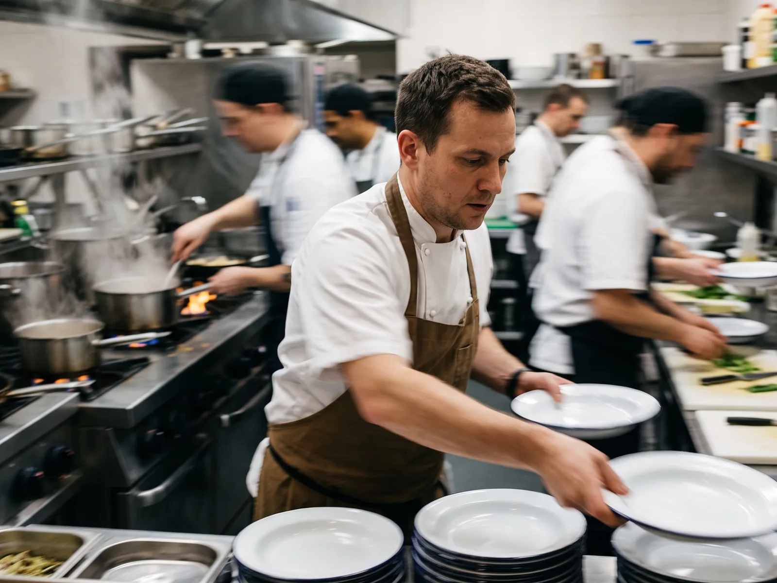 Brigade de restaurant en plein service, un chef saisissant une pile d'assiettes émaillées blanches à bordure noire