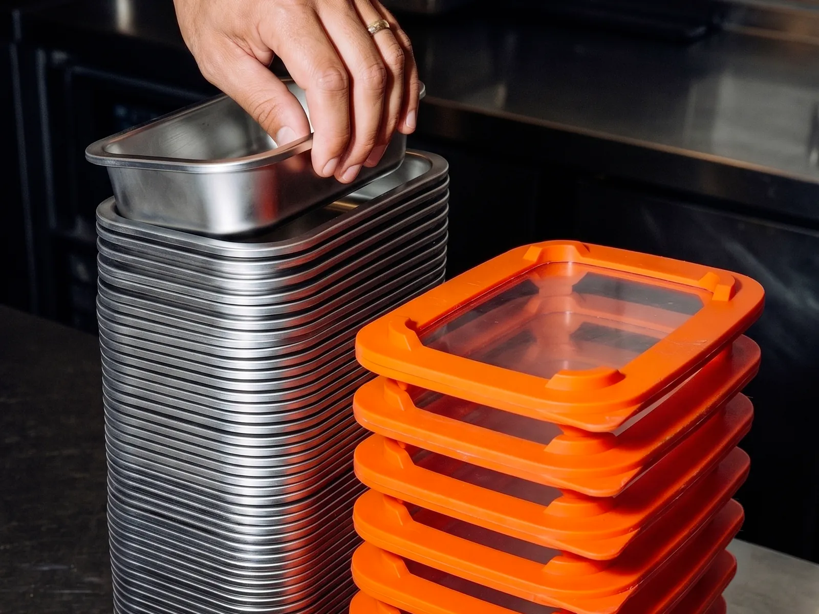 Barquettes inox RestoPep's emboîtées en pile serrée, couvercles orange empilés à part