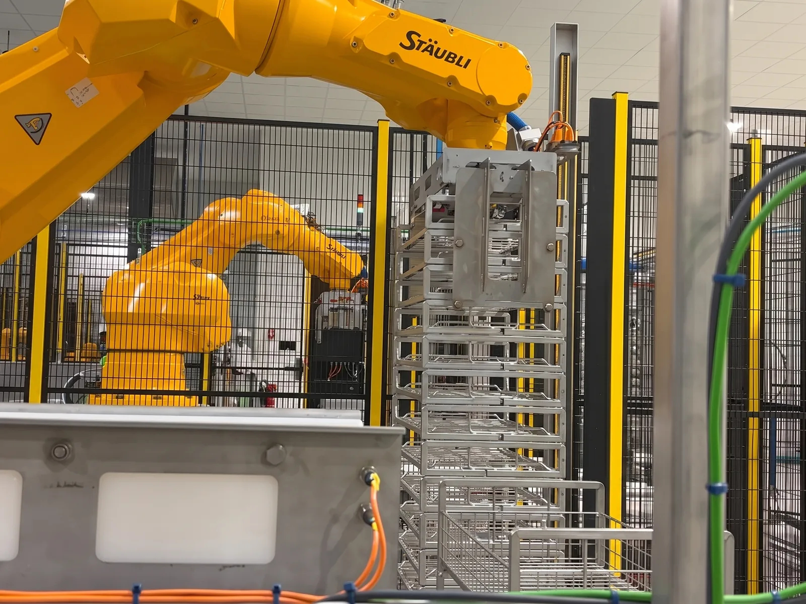 Bras robotisés manipulant une pile de caisses filaires inox sur une ligne de lavage automatisée