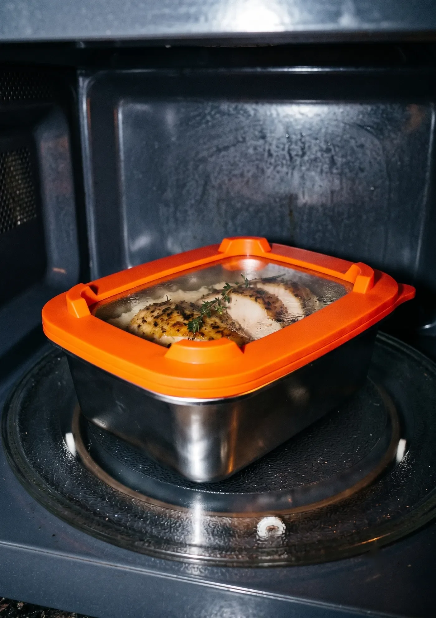 Barquette inox RestoPep's à couvercle orange en cours de réchauffe dans un micro-ondes
